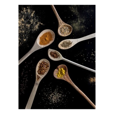 Six wooden spoons in a a circle with colourful spices on them and on the dark countertop.